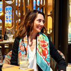 Woman wearing a colorful silk scarf with a pomegranate design in a restaurant setting. Silk scarf is reflecting the sophisticated lifestyle and the outfit, luxury product with an authentic story