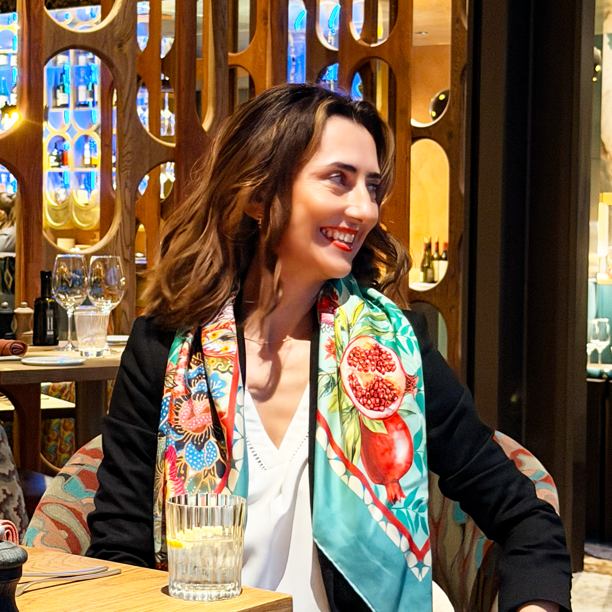 Woman wearing a colorful silk scarf with a pomegranate design in a restaurant setting. Silk scarf is reflecting the sophisticated lifestyle and the outfit, luxury product with an authentic story